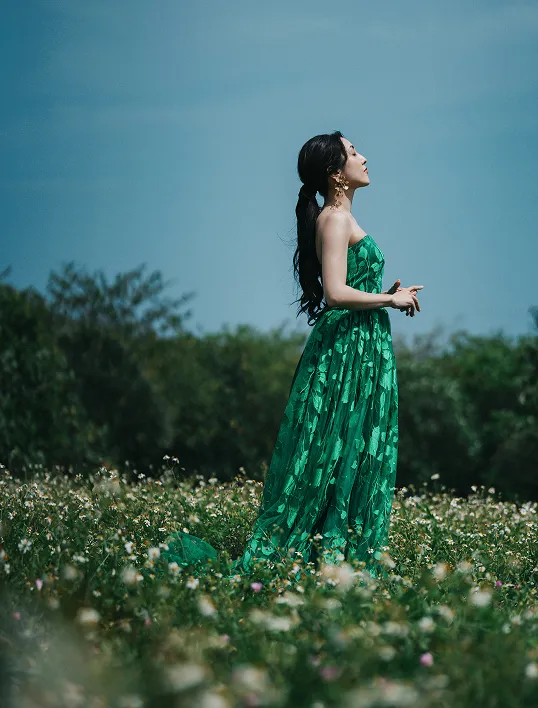 白い小花が一面に広がるお花畑に立ち、青空を見上げるLeafiaのドレス姿
