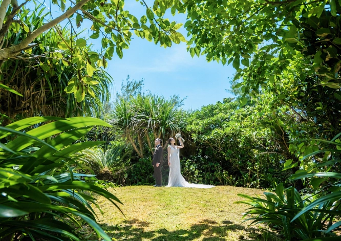 瀬良垣島の緑豊かなガーデンに立つ新郎新婦